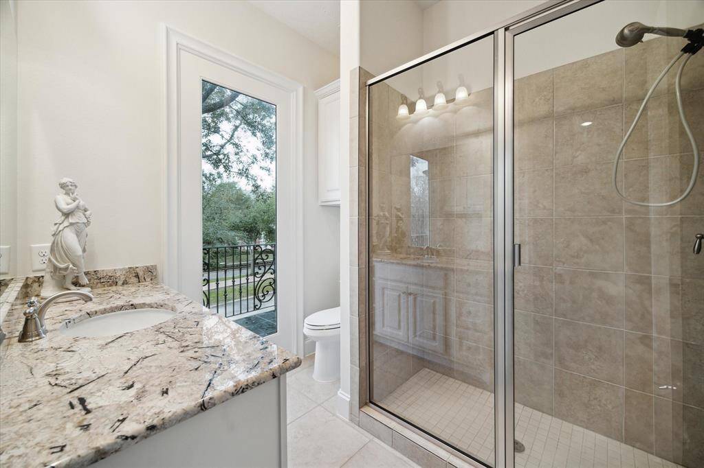EN SUITE BATH displays tile flooring, granite counter/backsplash, sink with painted cabinets below, fixed window looking out to outdoor balcony, built-in linen storage, mirror with light sconce, glass front walk-in shower with tile surround, recessed lighting, base molding.