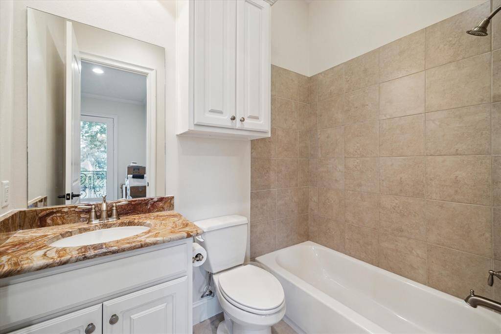 EN SUITE BATH includes tile flooring, stone counter/backsplash, sink with cabinet below, tub/shower with tile surround, built-in linen closet, mirror with light sconce above, base molding, recessed lighting,