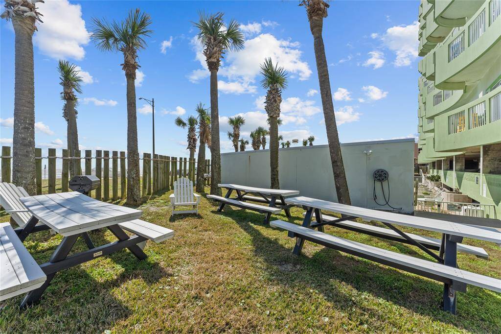 This outdoor space features a fenced-in area with palm trees, picnic tables, and a grill, creating a perfect setting for gatherings and relaxation.