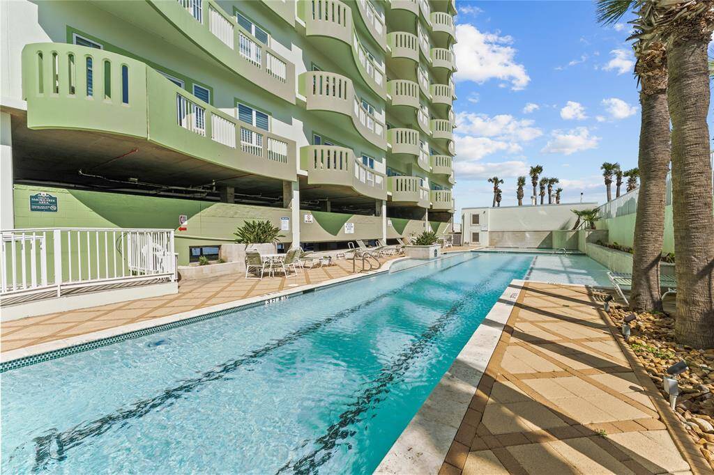 This photo showcases a luxurious outdoor swimming pool area with a modern design. Surrounded by palm trees, the pool area features ample deck space for lounging and is adjacent to workout room. Perfect for relaxation and entertaining.
