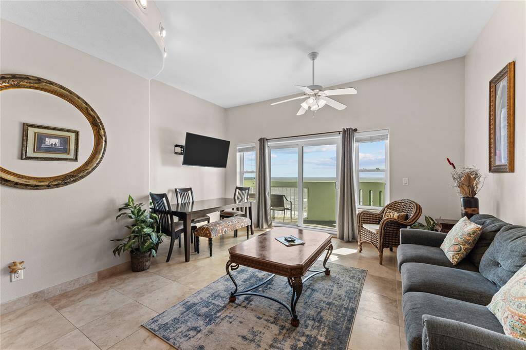 This bright, open-concept living area features tiled flooring, a ceiling fan, and ample natural light. The space includes a cozy seating area, a coffee table, Dining table.  Neutral tones and  décor create a welcoming atmosphere.