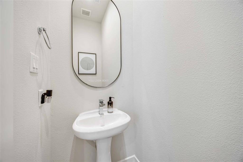 This is a compact, modern powder room featuring a sleek pedestal sink, oval mirror, and minimalist decor. Ideal for a contemporary home.