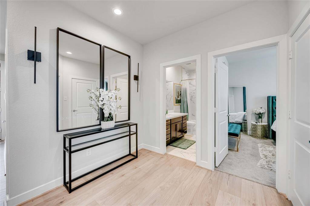 This photo showcases a bright and modern hallway with light wood flooring. It leads to a bathroom with contemporary fixtures and a bedroom with elegant furnishings.
