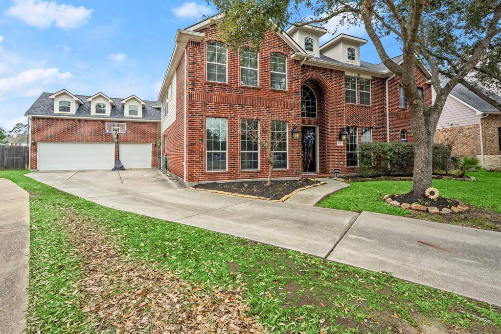 This is a spacious two-story brick home with a three-car garage and private drive. It features large windows, an elegant arched entryway, and a well-maintained front yard with mature trees and landscaping. The driveway provides ample parking space.