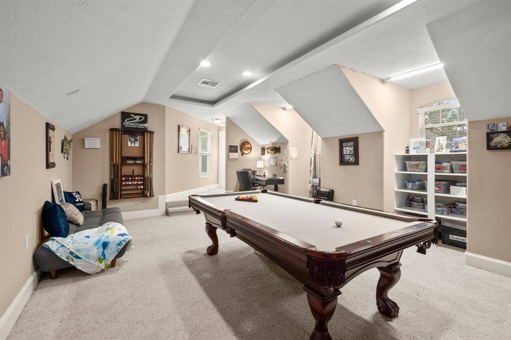 This spacious Media room features a pool table, cozy seating, and ample natural light. The angled ceiling and recessed lighting add character, while the wall shelves provide storage and display space. Perfect for entertainment and relaxation.
