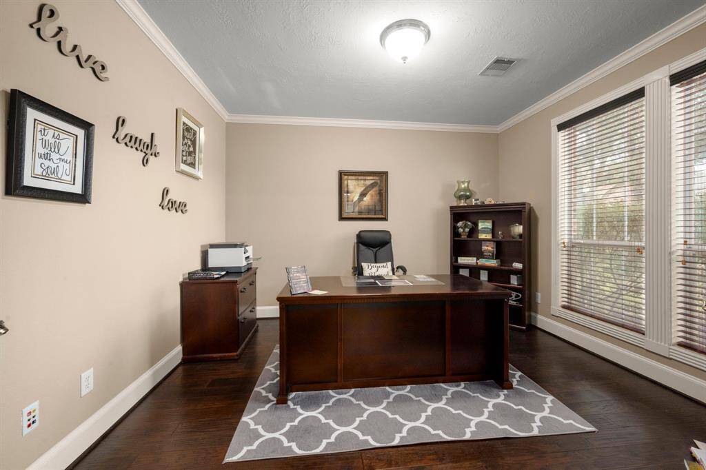 This photo showcases a well-lit home office featuring a large window with wooden blinds, hardwood flooring, and a dark wood desk. The walls are adorned with motivational decor, creating an inviting and productive workspace.