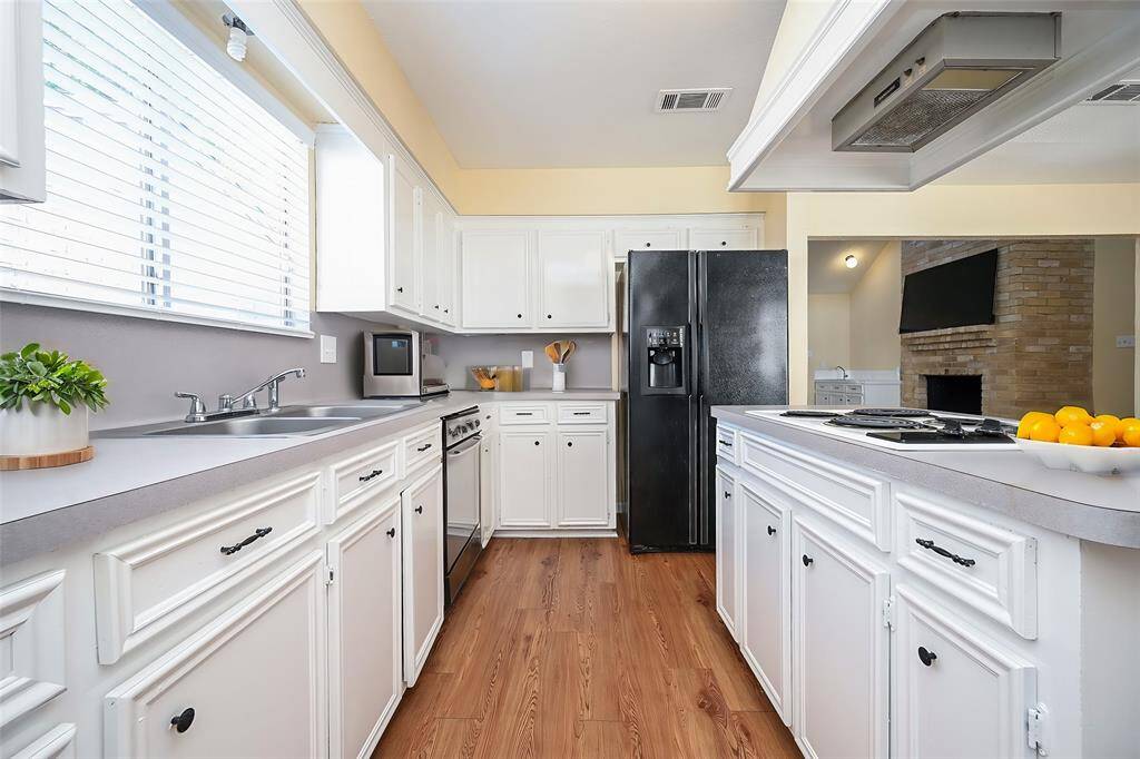 The photo showcases a bright, open-concept kitchen with modern appliances, ample cabinetry, and a ceiling fan, complemented by natural light from large windows and wood-look flooring.