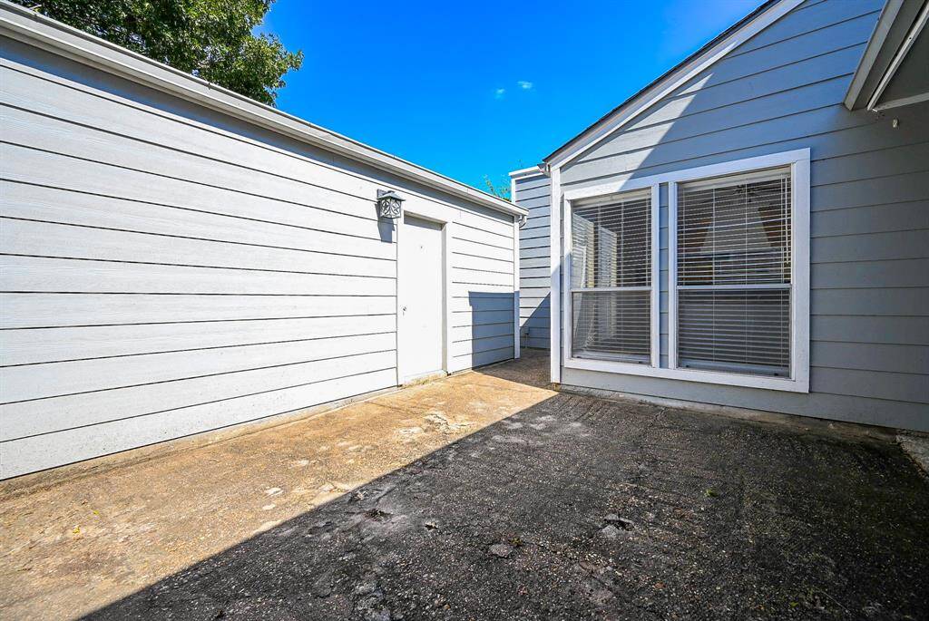 This is a side view of a property with a well-maintained brick pathway leading to a secure metal gate. On the left is a small garden area with mature flowering plants, and the home's exterior is finished with light siding.