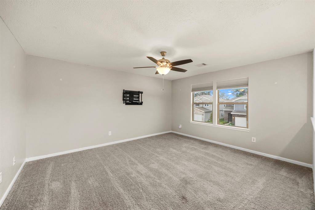 Spacious bedroom with neutral walls and carpet, featuring a ceiling fan and large windows offering plenty of natural light. Wall mount for TV included. Ideal for a cozy and comfortable living space.