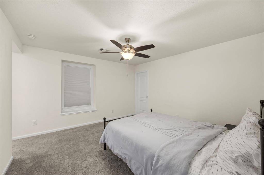 This bedroom features neutral walls and carpet, a ceiling fan, a single window, and a door. It's simply furnished with a bed, creating a cozy and functional space.