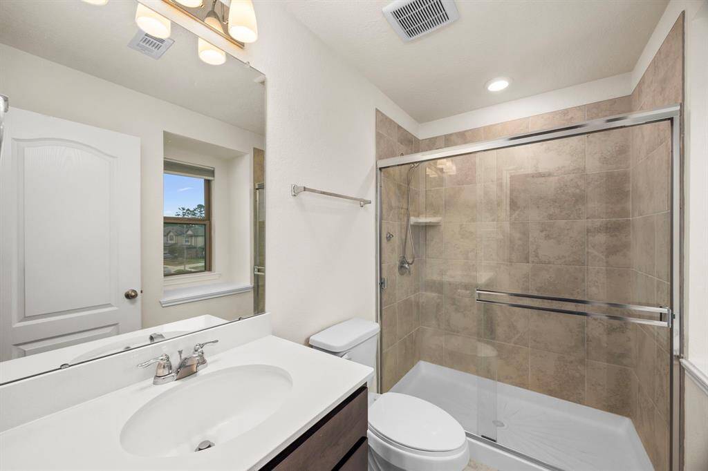 This bathroom features a modern design with a spacious glass-enclosed shower, a sleek vanity with a large mirror, and neutral tile work. Natural light streams in through a window, creating a bright and welcoming space.