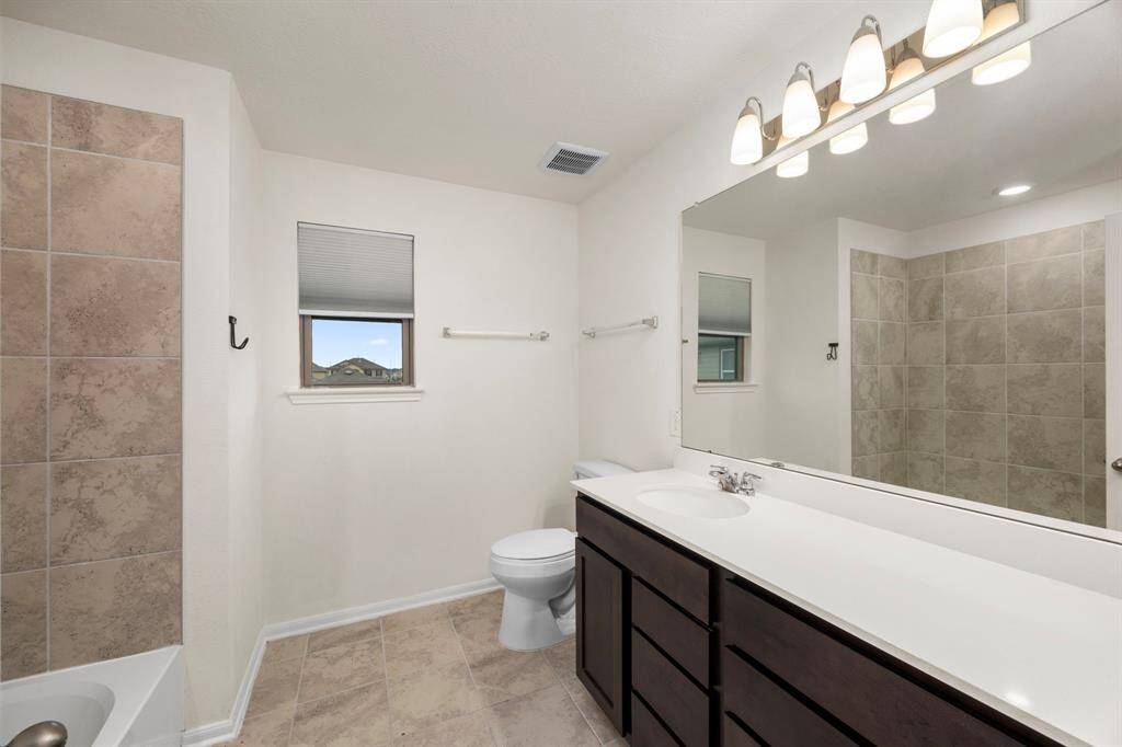This bathroom features a spacious layout with a double vanity, large mirror, and modern lighting. It includes a bathtub with tiled walls and a separate shower area. The neutral color palette and ample natural light create a clean and inviting atmosphere.