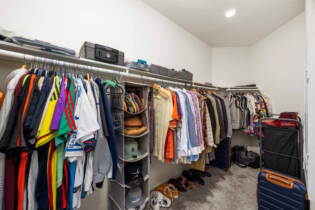 This photo features a spacious walk-in closet with ample hanging space and shelving, perfect for organizing clothes and accessories. The neutral tones and carpeted floor provide a clean and cozy feel.