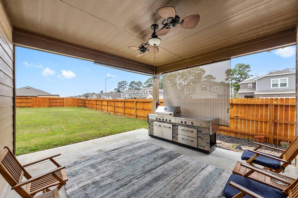 This photo showcases a spacious covered patio with a ceiling fan, outdoor grill setup, and seating. It overlooks a well-maintained fenced backyard, ideal for entertaining.