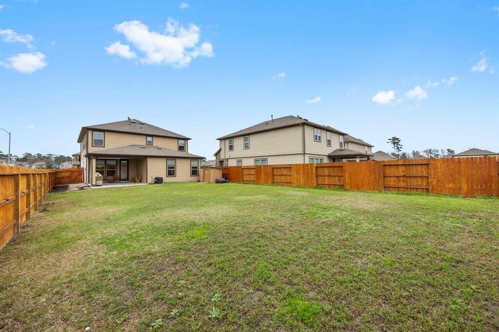 Spacious backyard with a well-maintained lawn, enclosed by a wooden fence. The two-story house features a covered patio area, ideal for outdoor activities and relaxation.