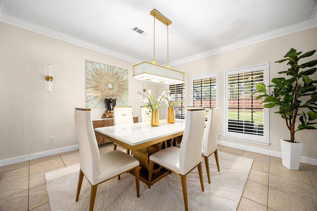 Experience modern elegance in this dining room, featuring a sleek white table, chic light fixture, and vibrant wall decor. Abundant natural light pours through large windows, complemented by a touch of greenery. Neutral tones create a warm, inviting atmosphere.