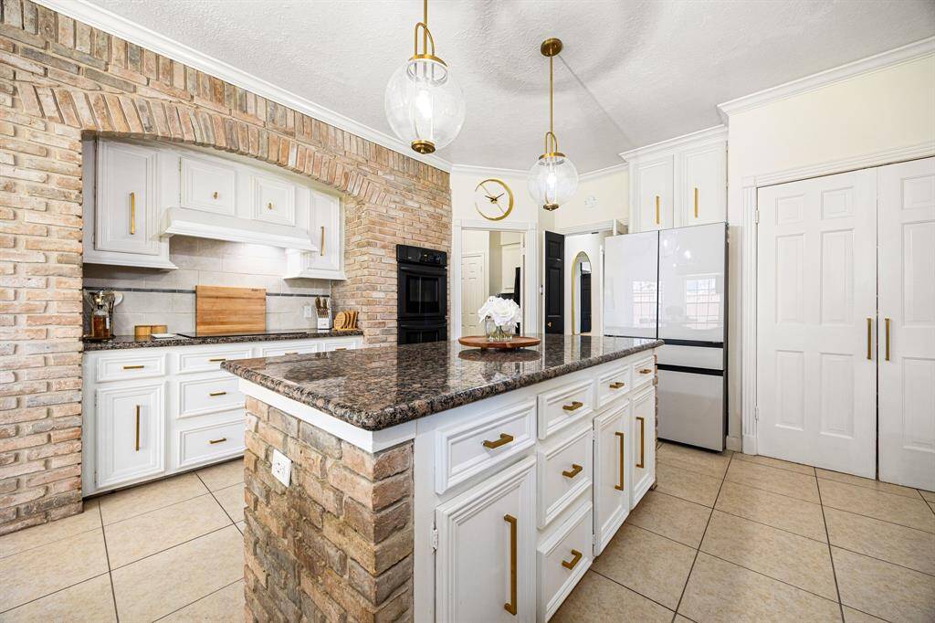This kitchen perfectly combines modern elegance and rustic charm, featuring exposed brick, sleek white cabinetry, and a spacious granite island. With contemporary pendant lighting and ample storage, it’s ideal for cooking and entertaining.