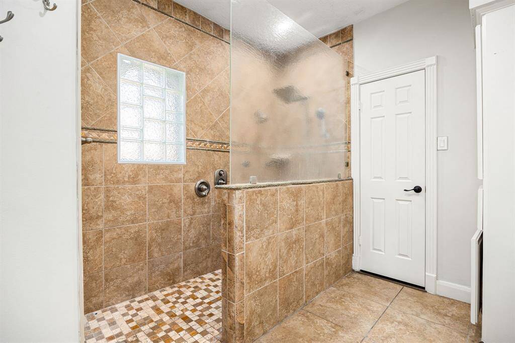 Experience luxury in this modern bathroom featuring a spacious walk-in shower with glass block and frosted glass for added privacy. The warm earth-tone tiles create a stylish and inviting atmosphere.