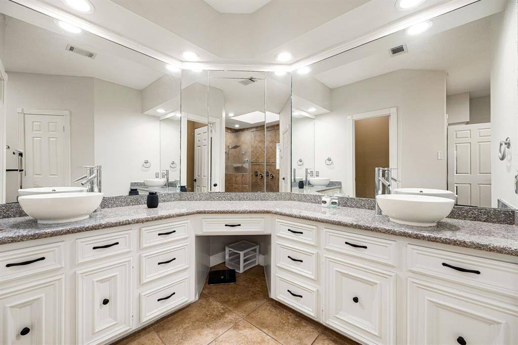 Experience luxury in this bathroom with a spacious double vanity, granite countertops, and elegant vessel sinks. Enjoy ample storage and a large mirror that brightens the space. Neutral tile flooring and white cabinetry create a sleek, modern aesthetic.