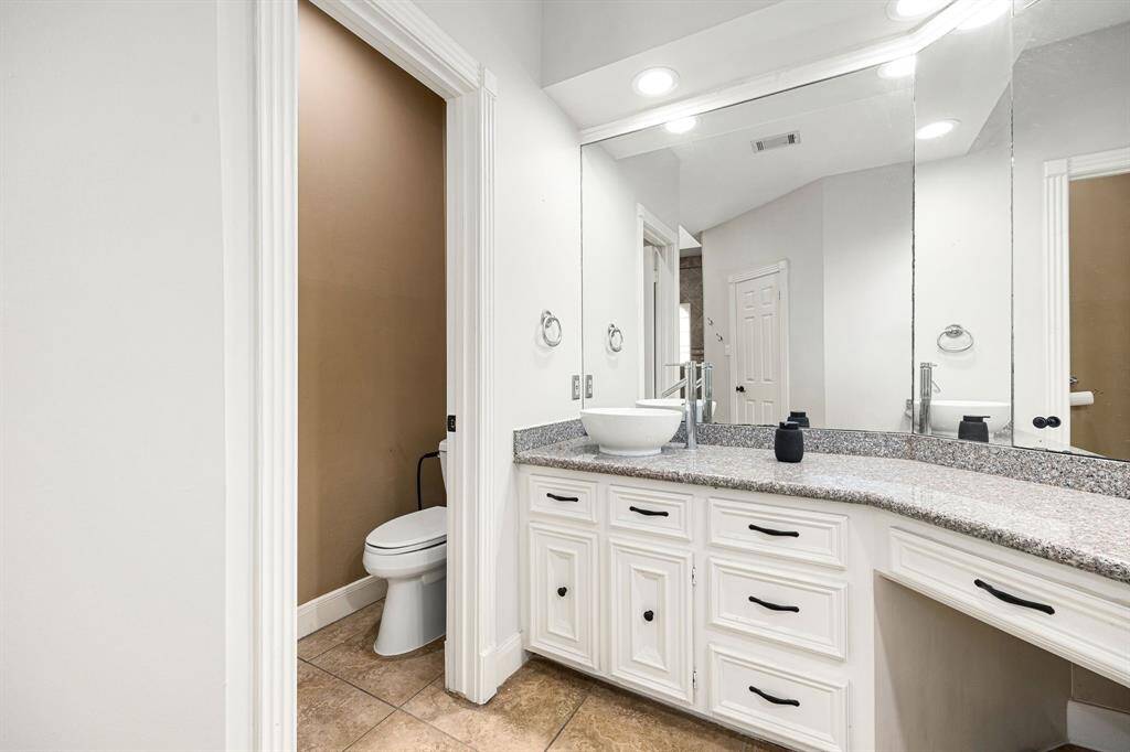 Sleek modern bathroom featuring a spacious granite vanity with ample storage, a stylish vessel sink, and a large mirror. Neutral tones and recessed lighting enhance the bright, clean atmosphere.