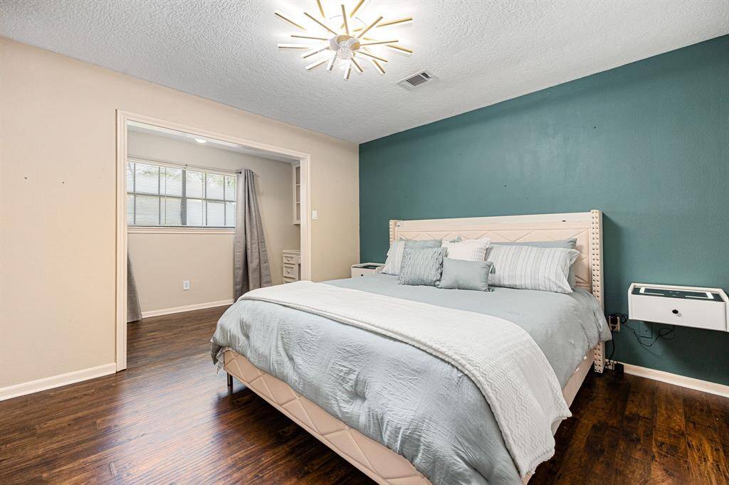 Charming bedroom with wood flooring, a stylish teal accent wall, and a modern light fixture. Enjoy a cozy bed and a bright bonus space with large windows.