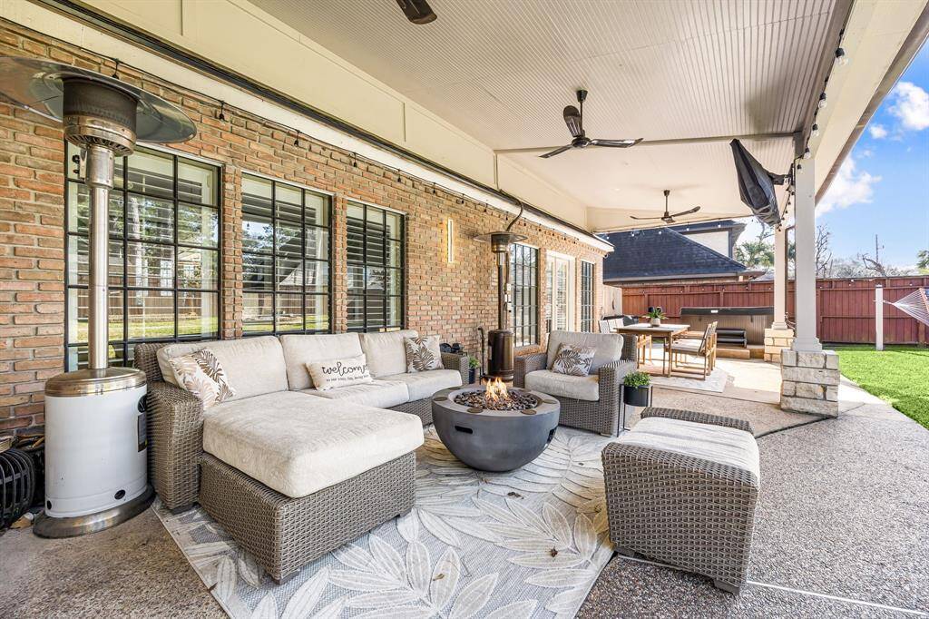 Discover the perfect outdoor retreat with this spacious covered patio, featuring a cozy seating area with a fire pit, outdoor heaters, ceiling fans, and a dining table. Ideal for entertaining or relaxation, it's beautifully lit and enclosed by a fenced yard.