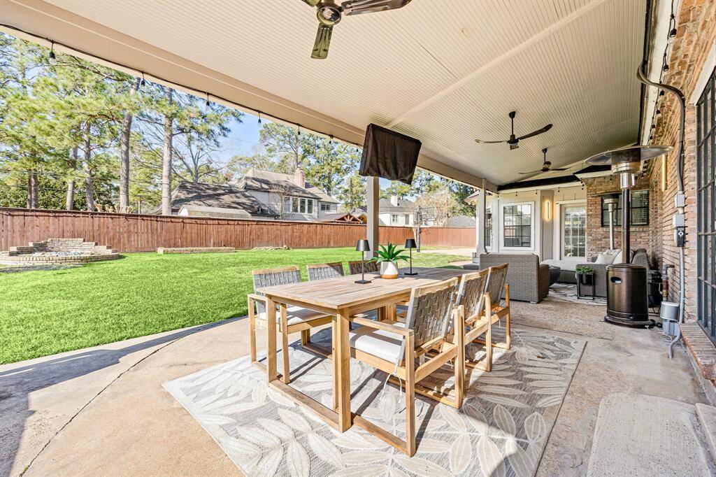 Enjoy outdoor living on this spacious, covered patio with a wooden dining set, ceiling fans, and a cozy seating area. The expansive backyard features a well-maintained lawn and a privacy-enhancing wooden fence, creating a serene retreat.