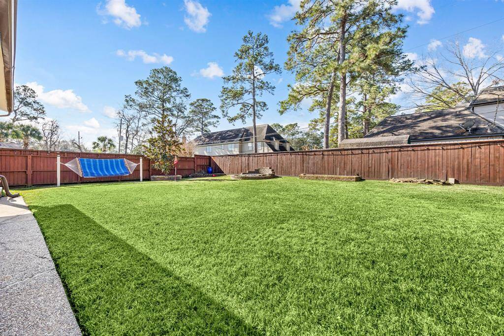 Expansive backyard with a lush lawn, private wooden fence, and mature trees offering ample shade. Includes a relaxing hammock—perfect for outdoor activities and entertaining.