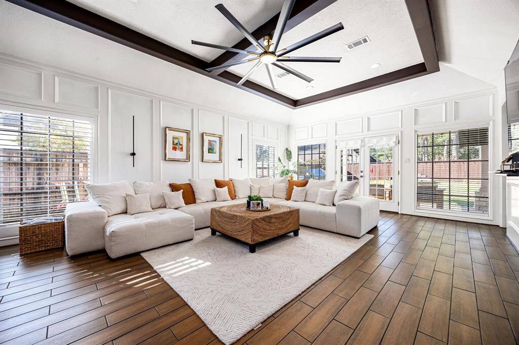 Experience the perfect blend of style and comfort in this bright, spacious living room featuring wood-look flooring, a chic sectional sofa, and a modern ceiling fan. Large windows and glass doors seamlessly connect to the backyard, flooding the space with natural light.