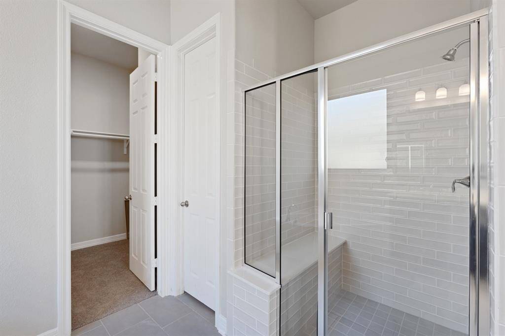 This additional view of your primary bathroom features tile flooring, fresh paint, walk-in shower, a separate garden tub, and a large walk-in closet.