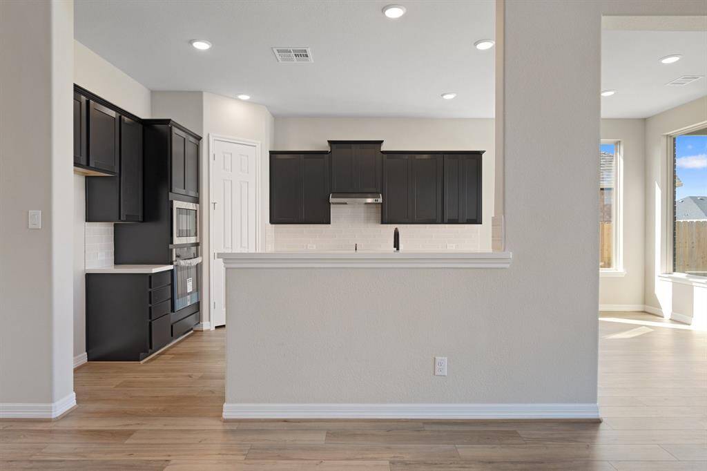 This light and bright kitchen features a large quartz island, dark stained cabinets, a large sink overlooking your family room, recessed lighting, and beautiful backsplash.