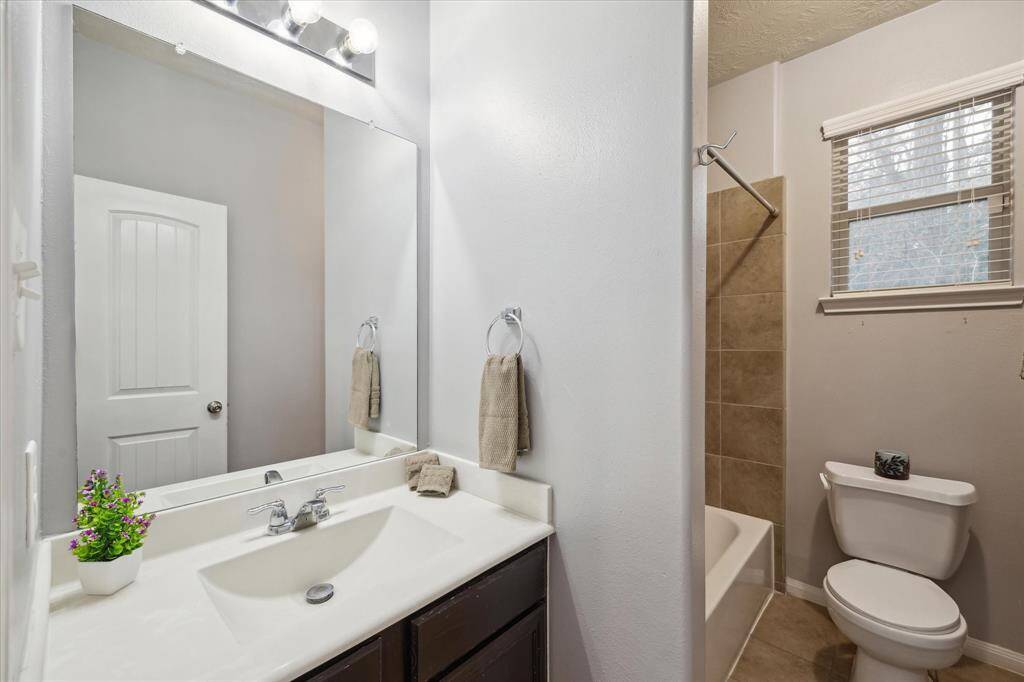 Secondary bath with neutral tones, featuring a large mirror, single sink vanity, and bathtub with a tiled shower area.