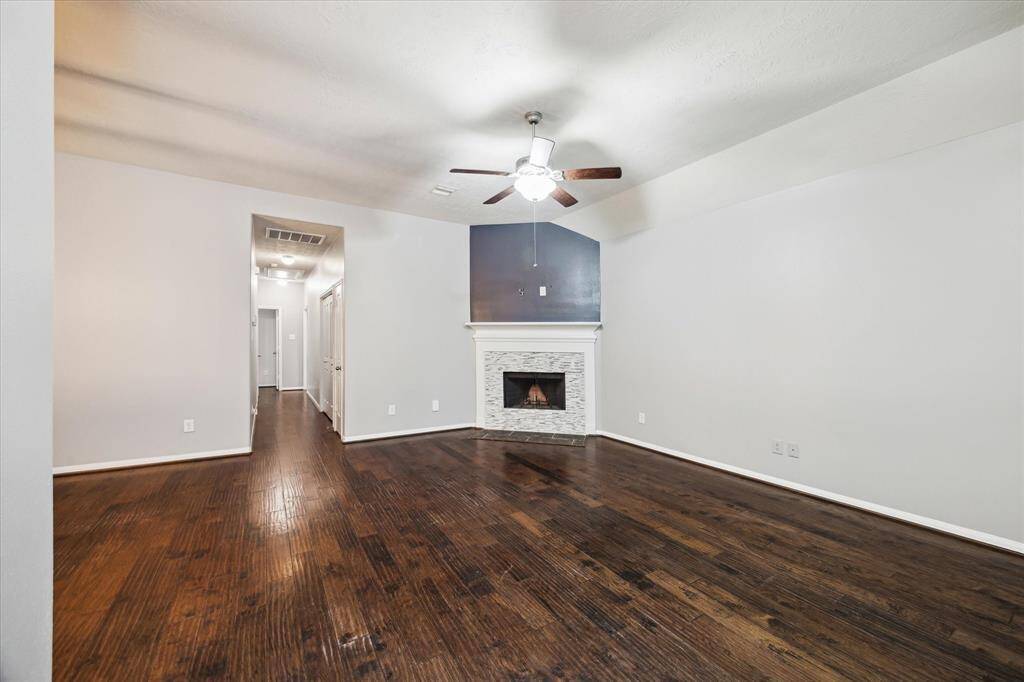 This spacious living room features rich hardwood floors, a warm gas fireplace, and a ceiling fan. The neutral walls and recessed lighting create a bright, inviting atmosphere.