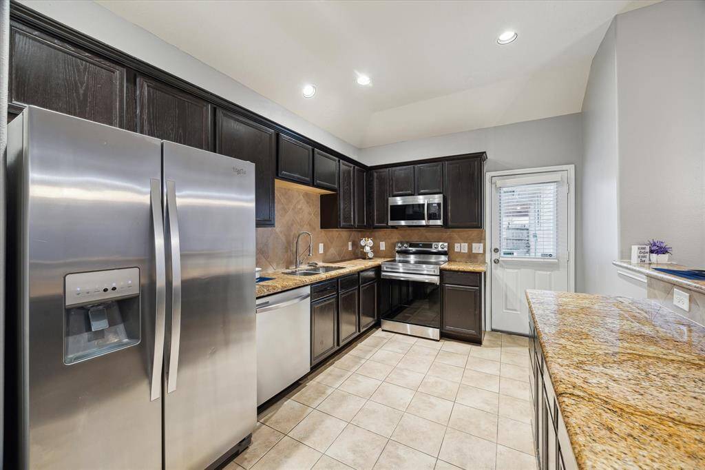 This kitchen features stainless steel appliances, dark wood cabinetry, and granite countertops. The space is well-lit with recessed lighting and has a tiled floor for easy maintenance.