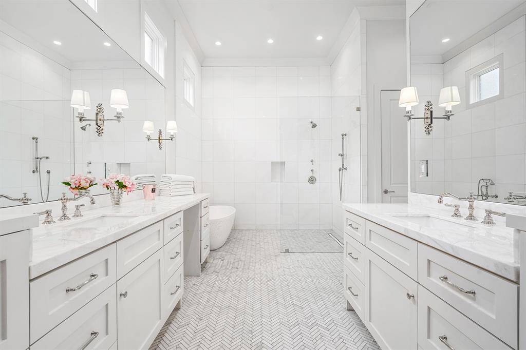 Primary suite features spa-like bath with stunning herringbone tiled floors, marble countertops, double vanities, ample storage, and designer sconces.