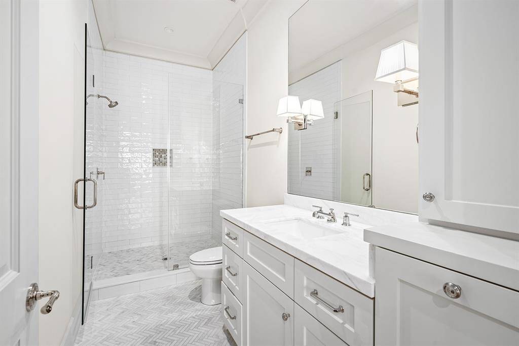 Secondary bathroom with beautiful sconces, herringbone tiled flooring, walk-in glass shower with floor to ceiling subway tile.