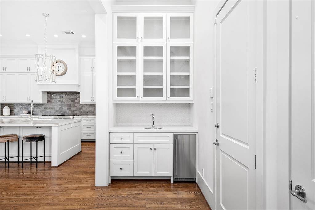 Wet bar conveniently located between kitchen and dinings area with Scotsman ice-maker, sink, glass cabinetry, and tile backsplash.