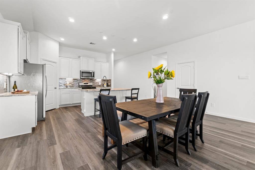 This is a bright, modern open-concept kitchen and dining area featuring white cabinetry, stainless steel appliances, and a stylish backsplash. Lots of natural lighting throughout.