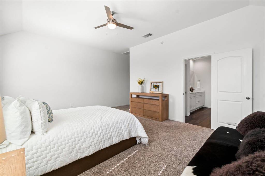Spacious and well-lit primary bedroom with neutral walls, plush carpeting, a modern ceiling fan, and an ensuite bathroom.