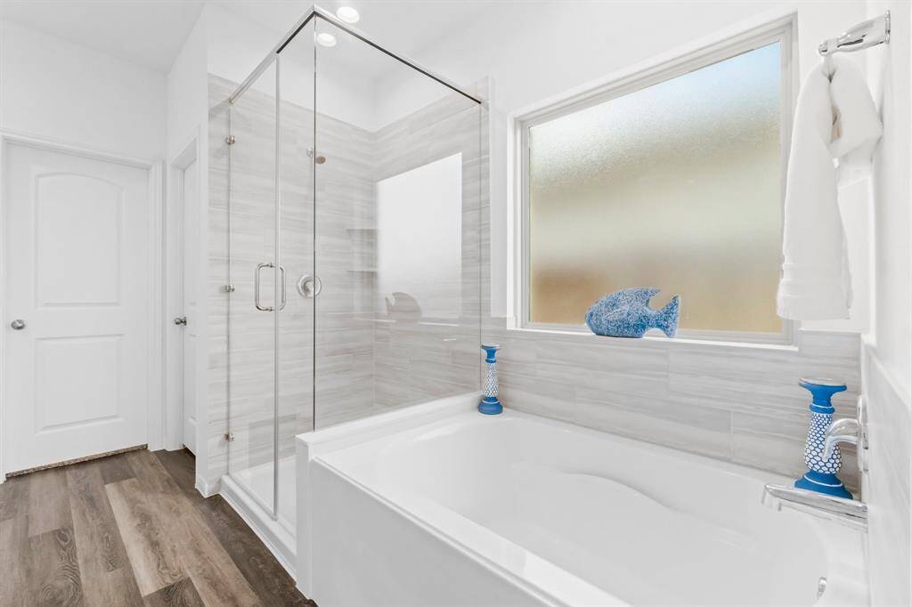 This modern bathroom features a glass-enclosed shower, a separate bathtub with stylish tile surround, and frosted privacy window. It's finished with wood-look flooring and crisp white walls.