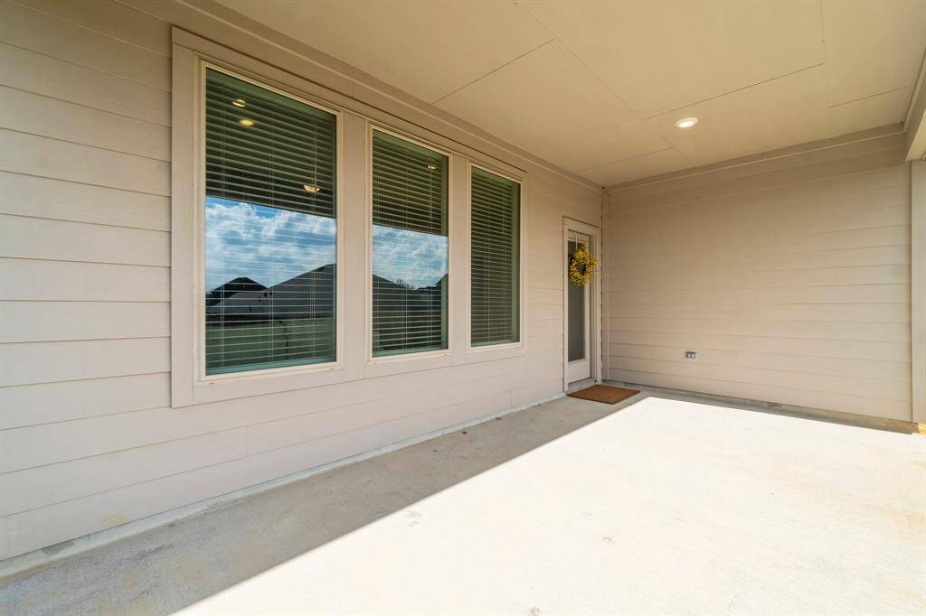This is an extended covered patio area featuring large windows, a recessed lighting fixture, and a welcoming back door. The patio offers ample space for outdoor furniture, making it an ideal spot for relaxation or entertaining guests.