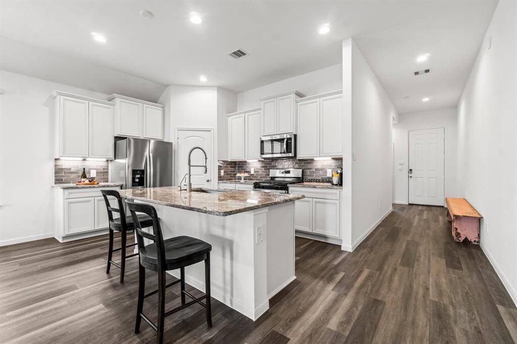 Modern kitchen featuring white cabinetry, stainless steel appliances, a bar seating area, and dark wood-like flooring. The clean, bright space includes recessed lighting and a neutral backsplash.