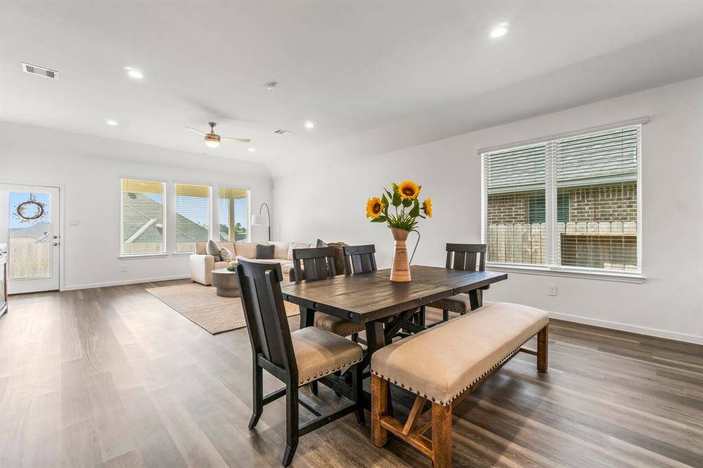 This is a spacious, well-lit dining and living area with modern fixtures, large windows, and light wood flooring, leading to an inviting private backyard oasis.