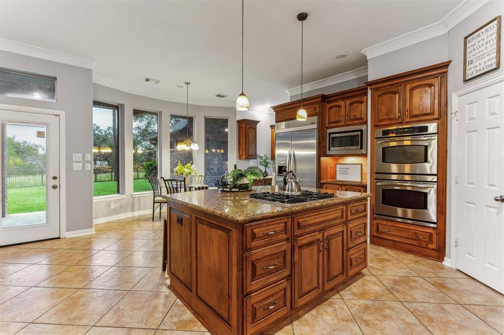 7014 Lake Haven Ct, Sugar Land Tx 77479-This luxurious kitchen is a chef's dream, featuring rich wooden cabinetry that provides ample storage space and a warm, inviting atmosphere. The centerpiece of the kitchen is a large granite island, perfect for meal preparation and casual dining, illuminated by elegant pendant lighting. The island also offers additional seating, making it a functional and social hub of the home.
