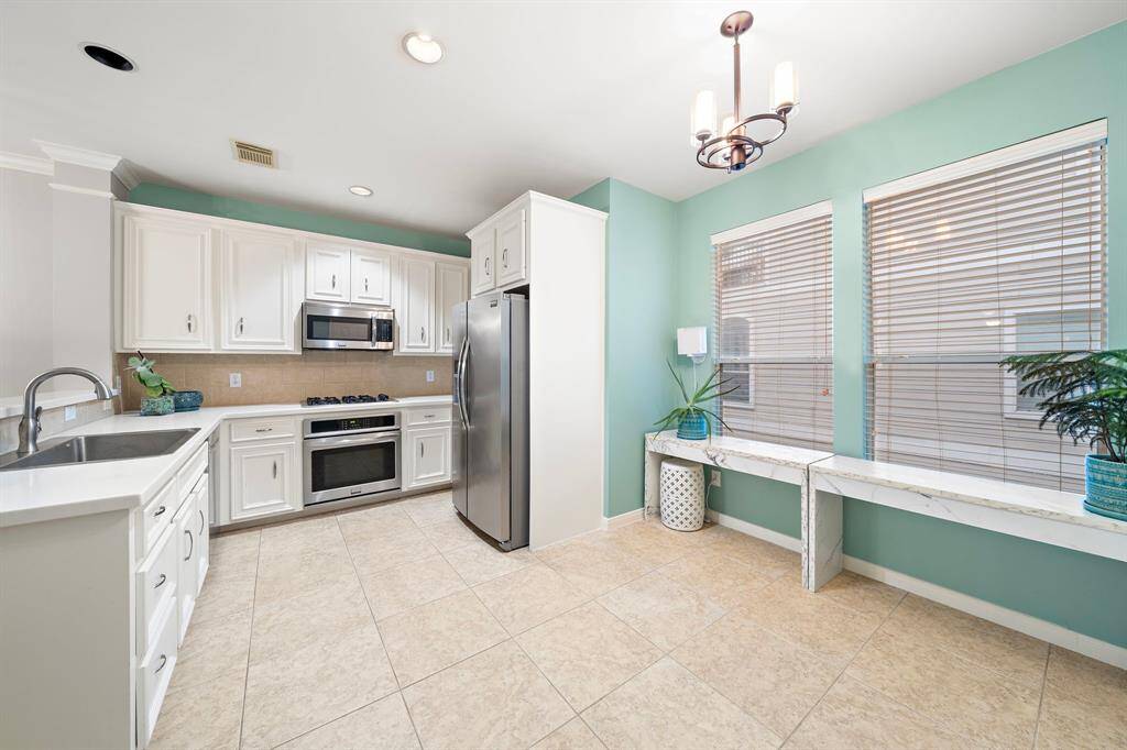 White cabinets line the kitchen, alongside stainless steel appliances & a cooktop. Tile floors extend into the breakfast area, offering convenient access to the kitchen.