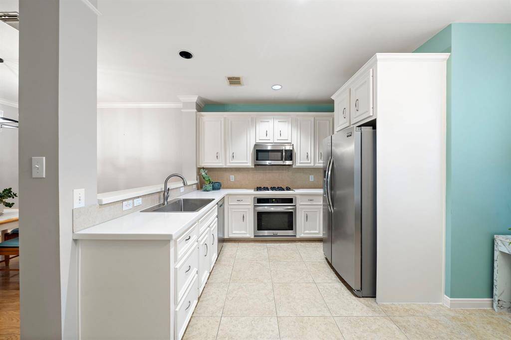 White cabinets and stainless-steel appliances define this efficient kitchen. Neutral tile flooring extends throughout, while a breakfast bar enhances the space for informal meals.