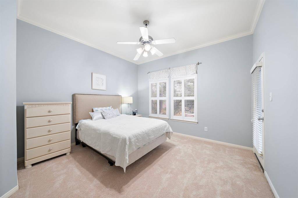 Carpeted secondary bedroom featuring an ensuite bath and backyard views via shuttered windows.