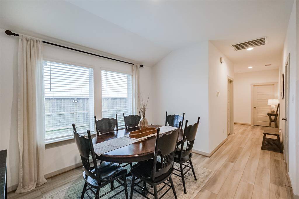 A light and bright dining area features large side facing windows with curtains for natural light, as well as easy maintenance luxury vinyl plank floors, neutral paint, and a seamless trasnsition into the adjoining kitchen and living area.