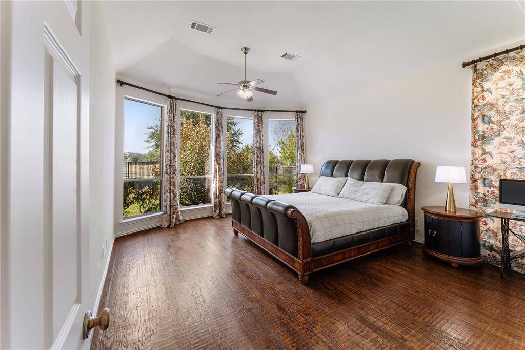 The luxurious primary suite boasts rich hardwood flooring, complemented by a soaring tall ceiling that adds an airy, open feel. A beautiful bay window enhances the space, flooding the room with natural light and offering a peaceful view of the surroundings.