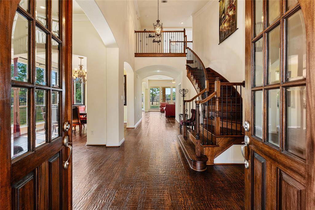 The grand entryway boasts stunning hardwood floors and soaring tall ceilings, creating an open and inviting atmosphere. A curved staircase with elegant wrought iron spindles gracefully leads upstairs, while large windows provide captivating views straight to the peaceful backyard.